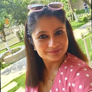 Roy smiling outdoors with sunglasses on her head, wearing a pink polka dot blouse.