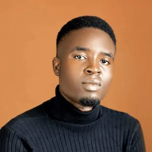 Samuel posing for a photo against a warm orange background, wearing a black turtleneck sweater.